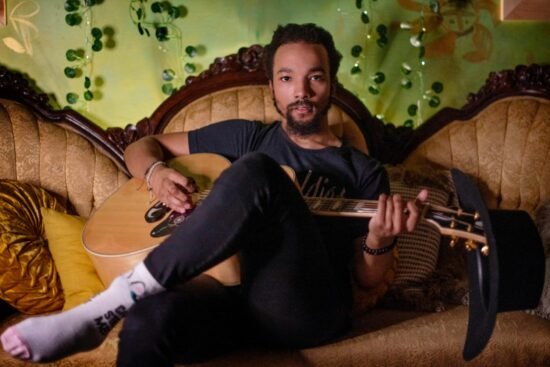 Dwayne Haggins avec sa guitare dans un canapé